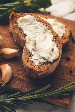 Board with slices of fresh bread and garlic butter on light wooden background, closeup