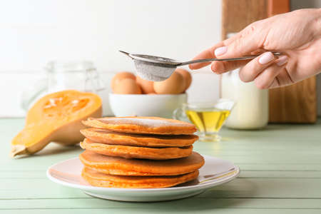 Woman sprinkling sugar powder onto tasty pumpkin pancakes on plateの写真素材
