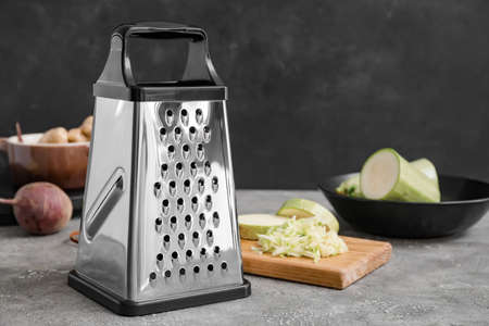 Metal grater and vegetables on dark background