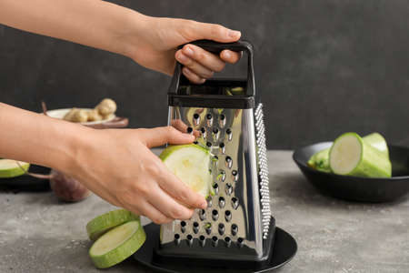 Woman grating zucchini on dark backgroundの写真素材