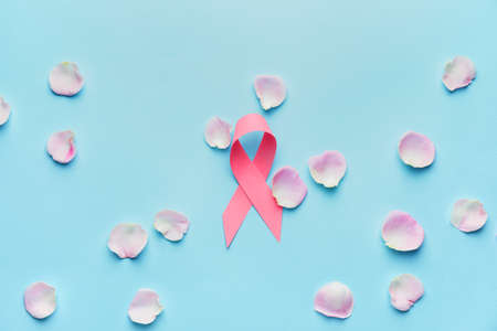 Pink ribbon and rose petals on color background. Breast cancer awareness concept