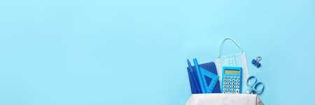 Pencil case with stationery and medical mask on color background with space for text