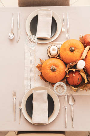 Beautiful table setting with pumpkins and autumn leaves in dining roomの写真素材