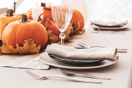Beautiful table setting with pumpkins and autumn leaves in dining roomの写真素材