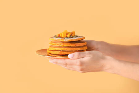 Hands with plate of tasty pumpkin pancakes on color background
