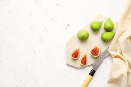 Board with fresh green figs and knife on light background