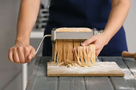 Woman making pasta with machine at table in kitchen