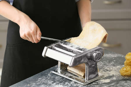 Woman making pasta with machine at table in kitchen
