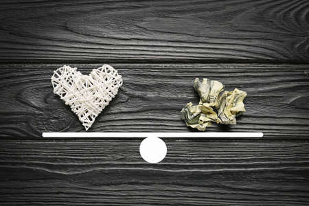 Crumpled banknote and heart on teeterboard against wooden background. Concept of balanceの写真素材