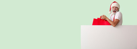 Surprised Santa Claus with blank poster and shopping bags on color background with space for textの写真素材