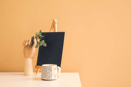 Wooden hand with chalkboard and cup on table near color wall in room