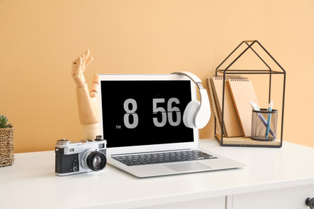 Wooden hand with laptop and photo camera on table near color wall in room
