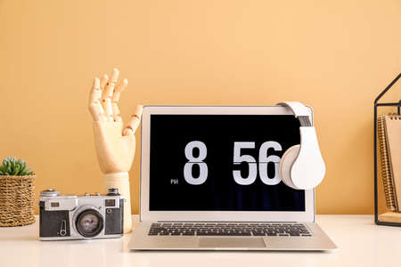 Wooden hand with laptop and photo camera on table near color wall in room