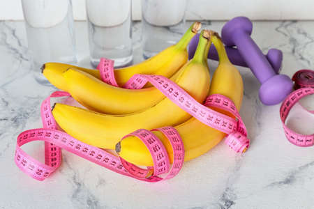 Ripe bananas, measuring tape and dumbbells on light background. Weight loss concept