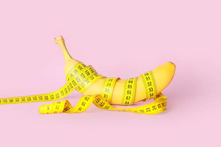 Ripe banana and measuring tape on color background. Weight loss conceptの写真素材