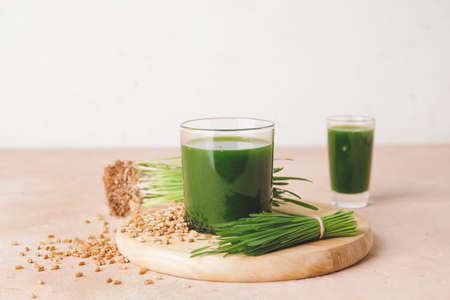 Glass with fresh wheatgrass juice on light background