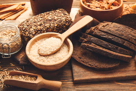 Different cereals and bread on wooden background, closeup