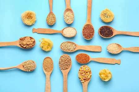 Spoons with different cereals and raw pasta on color backgroundの写真素材