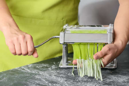 Woman making pasta with machine at tableの写真素材