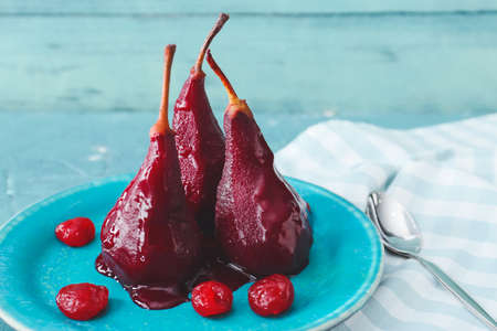 Plate of tasty poached pears in wine sauce on color wooden background