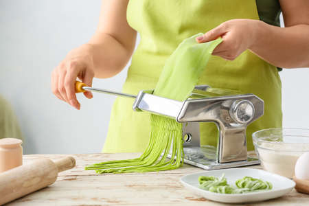 Woman making pasta with machine at tableの写真素材