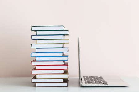 Stack of books and laptop on table against light wallの写真素材