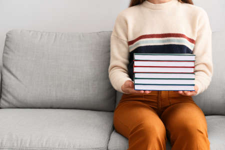 Woman with stack of books sitting on sofaの写真素材