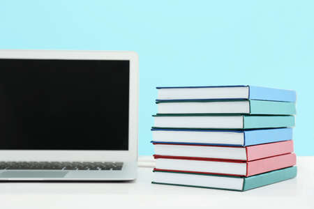 Stack of books and laptop on table against color wallの写真素材