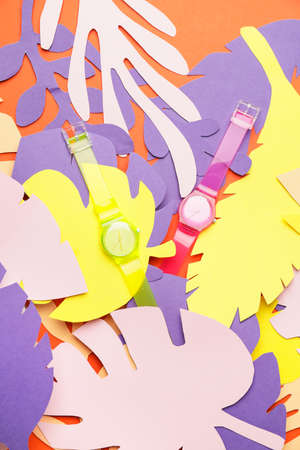Wrist watches with paper tropical leaves on color background