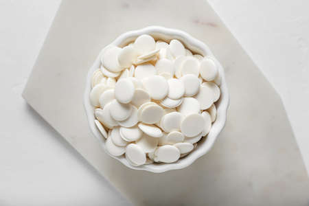 Bowl with chocolate drops on light background