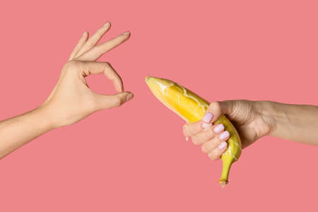 Female hands with banana in condom and with liquid on color background.の写真素材