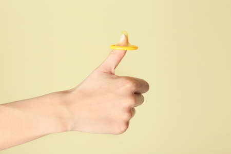 Female hand with condom showing thumb-up gesture on color background.の写真素材