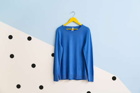 Hanger with stylish sweater on color background