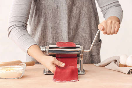 Woman making dough for pasta with machine at tableの写真素材