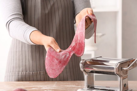 Woman making dough for pasta with machine at tableの写真素材