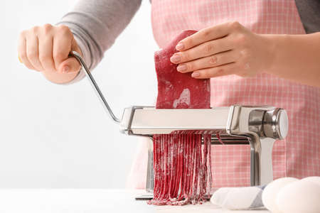 Woman making noodles with pasta machine at tableの写真素材