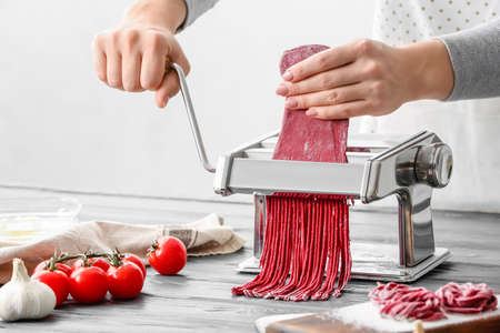 Woman making noodles with pasta machine at tableの写真素材