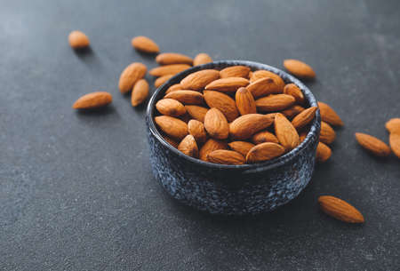 Bowl with healthy almonds on dark background