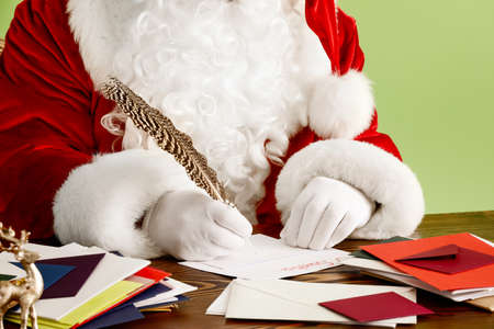 Santa Claus making list of gifts on color background