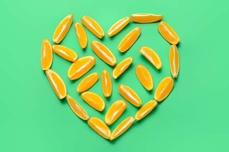 Heart made of cut oranges on color background