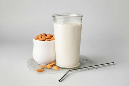 Glass of tasty almond milk and bowl with nuts on light backgroundの写真素材