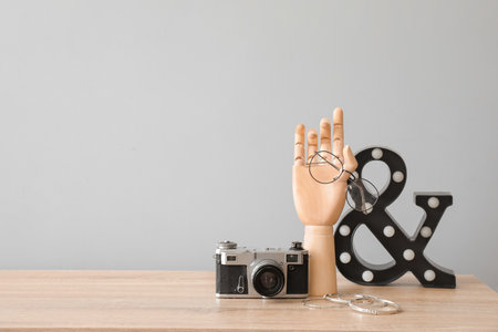 Wooden hand with photo camera, eyeglasses and jewelry on table in interior of roomの写真素材