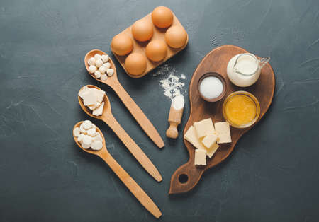 Spoons with chocolate drops and ingredients for bakery on dark background