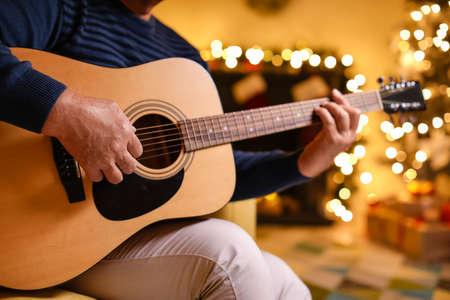 Mature man playing guitar at home on Christmas eveの写真素材