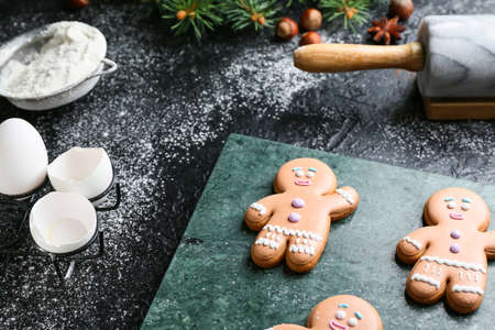 Tasty gingerbread cookies and ingredients on dark background