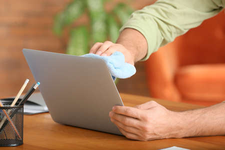 Young man cleaning laptop at home, closeup