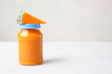 Jar with healthy baby food and slice of pumpkin on light backgroundの写真素材