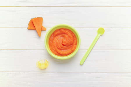 Bowl with pumpkin baby puree, spoon and pacifier on white wooden backgroundの写真素材