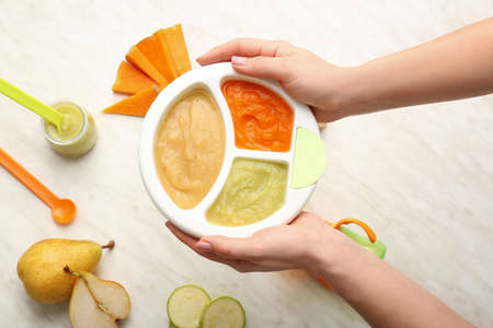 Woman holding plate with different baby food on light backgroundの写真素材