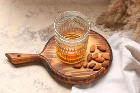 Board with glass of almond liquor and nuts on grunge background
